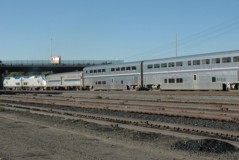 A silver Amtrak passenger train sits on tracks at a station, illustrating rail travel infrastructure.