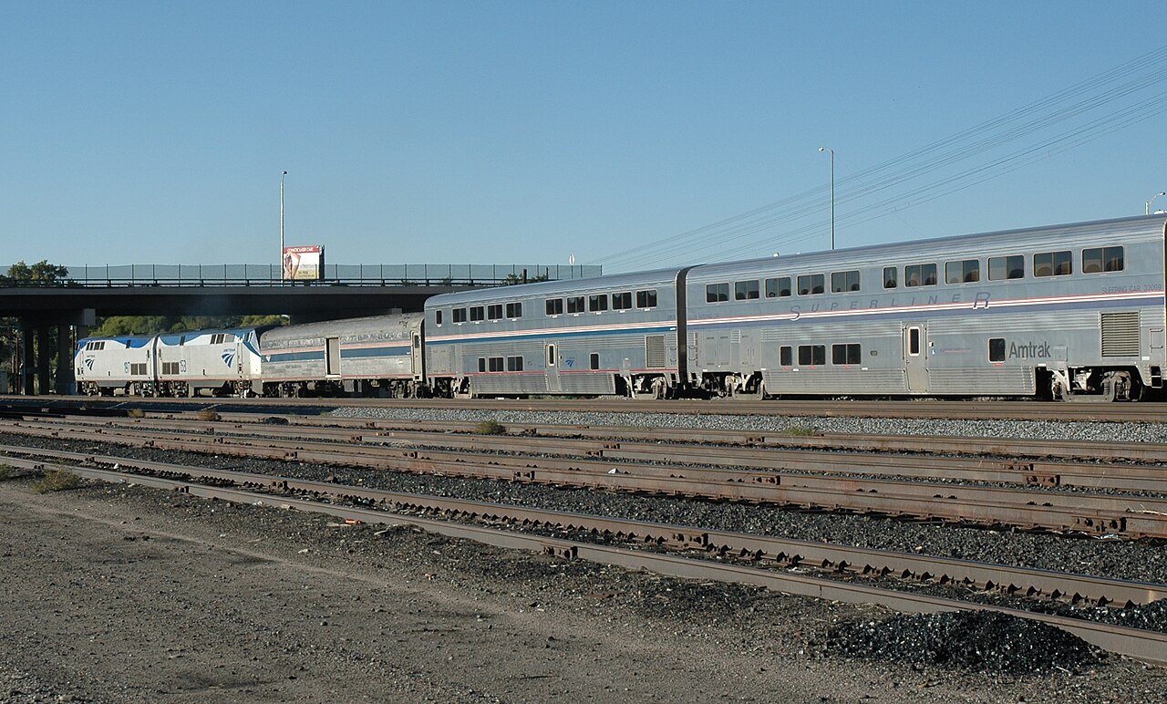 A silver Amtrak passenger train sits on tracks at a station, illustrating rail travel infrastructure.