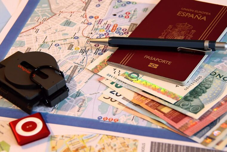 A passport, pen, map, and various currencies laid out on a table for travel planning.