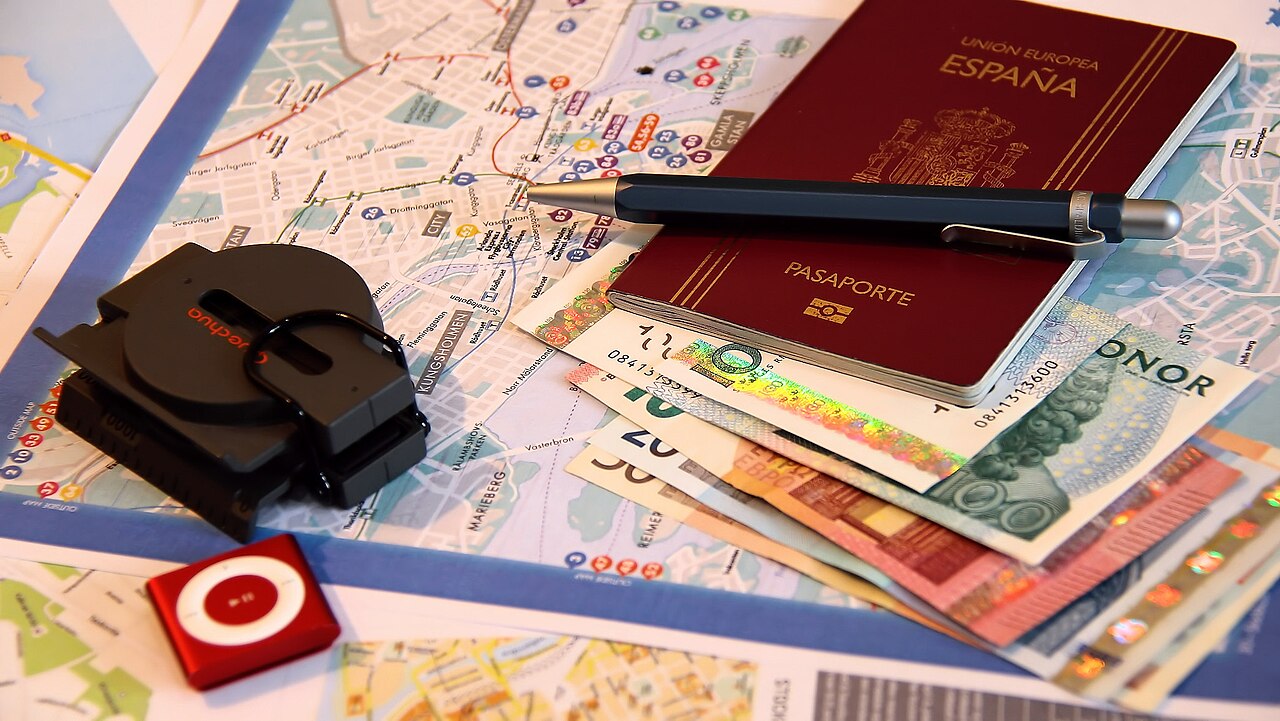 A passport, pen, map, and various currencies laid out on a table for travel planning.