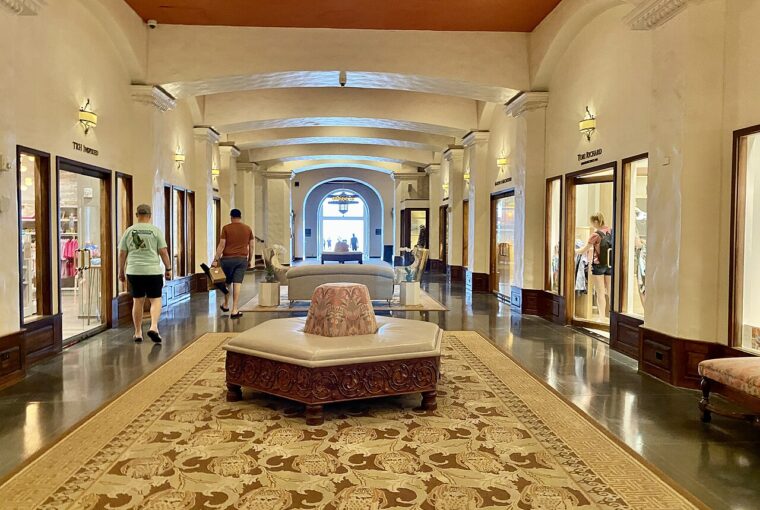 A wide hallway in a historic hotel lobby with polished floors, arched doorways, and guests walking through.