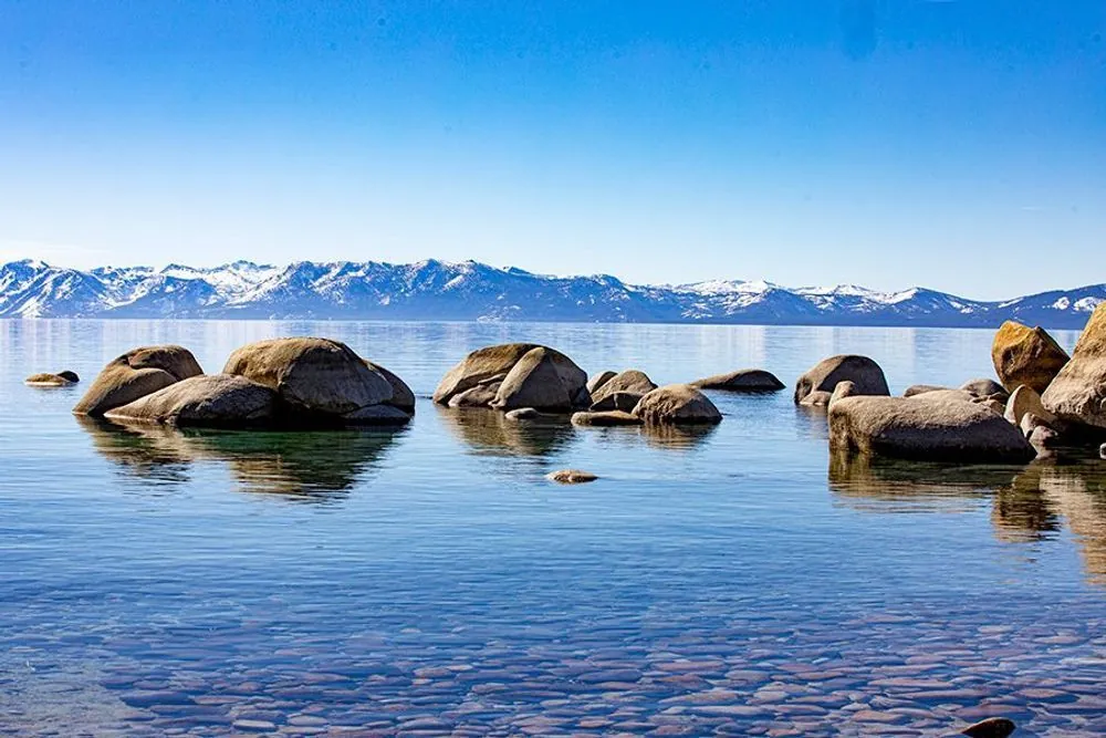 Granite boulders reflected in clear Lake Tahoe water beneath snow-covered Sierra Nevada mountains