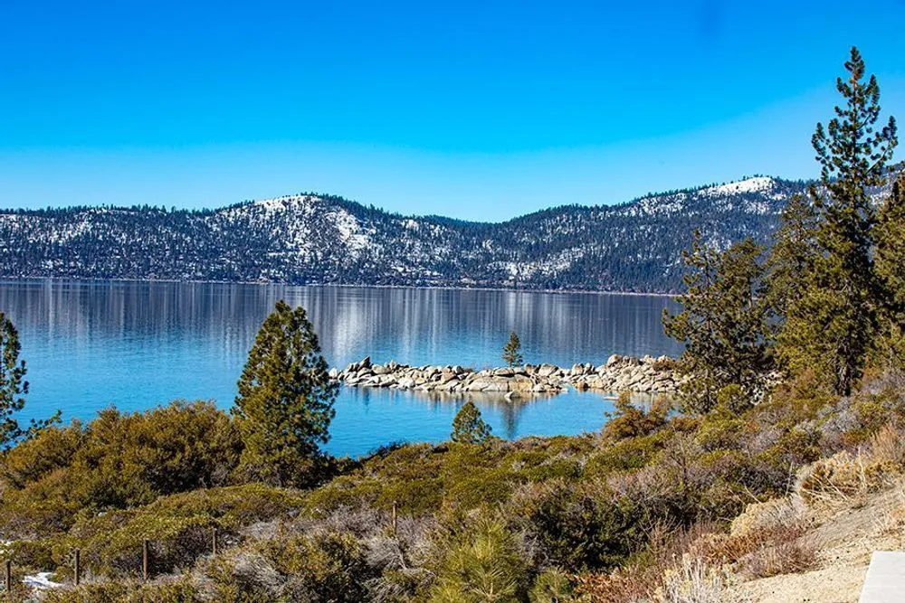 Pines and a rocky Lake Tahoe cove with blue water and snow-dusted forested slopes