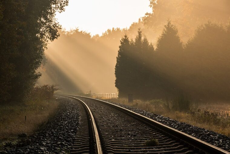 Sunlight streams through trees onto railway tracks during a misty, golden autumn morning.