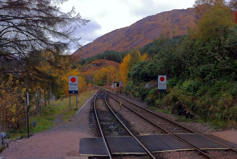 Railway tracks curving through a landscape with autumn foliage and mountains under a cloudy sky