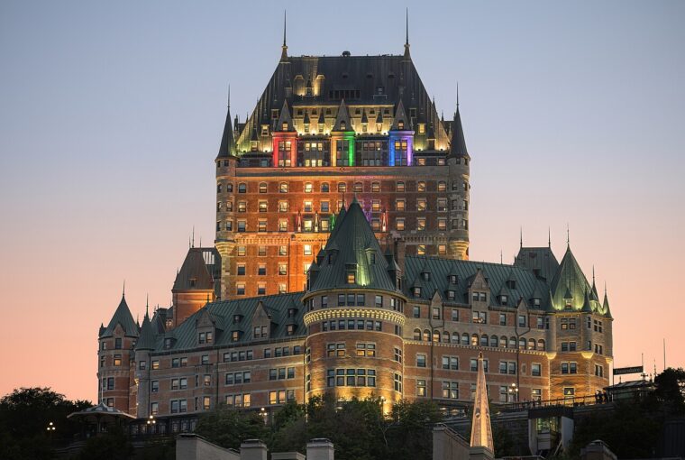 The historic Fairmont Le Château Frontenac hotel stands illuminated against a soft, twilight sky in Quebec City.