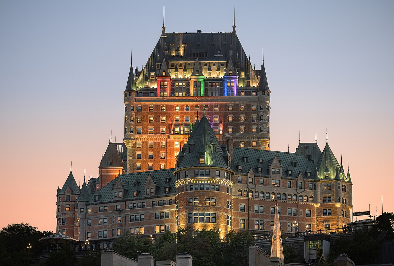 The historic Fairmont Le Château Frontenac hotel stands illuminated against a soft, twilight sky in Quebec City.
